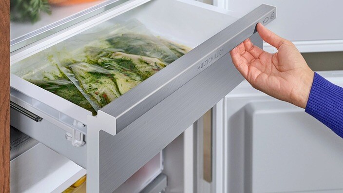 A hand is opening a drawer in a fridge-freezer.