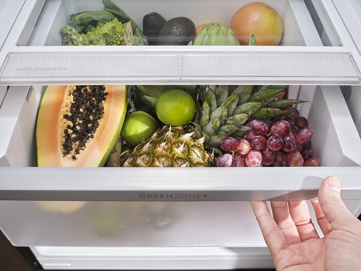 Different types of fruits and vegetables are placed in a drawer in a fridge-freezer.