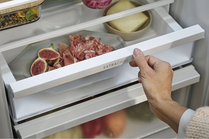 A hand is opening a drawer in a fridge-freezer.