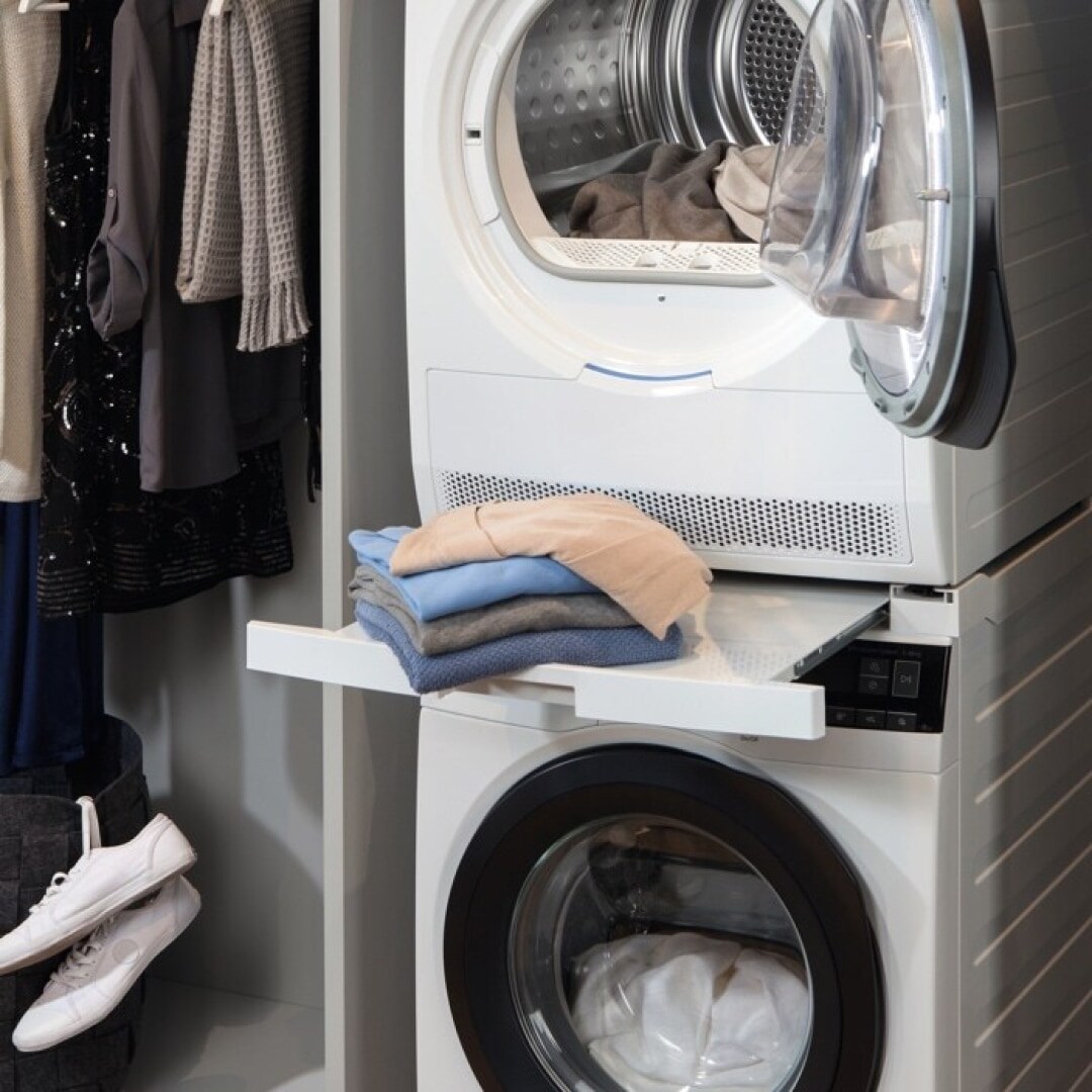 A washing machine and a tumble dryer stacked next to hanging clothes.
