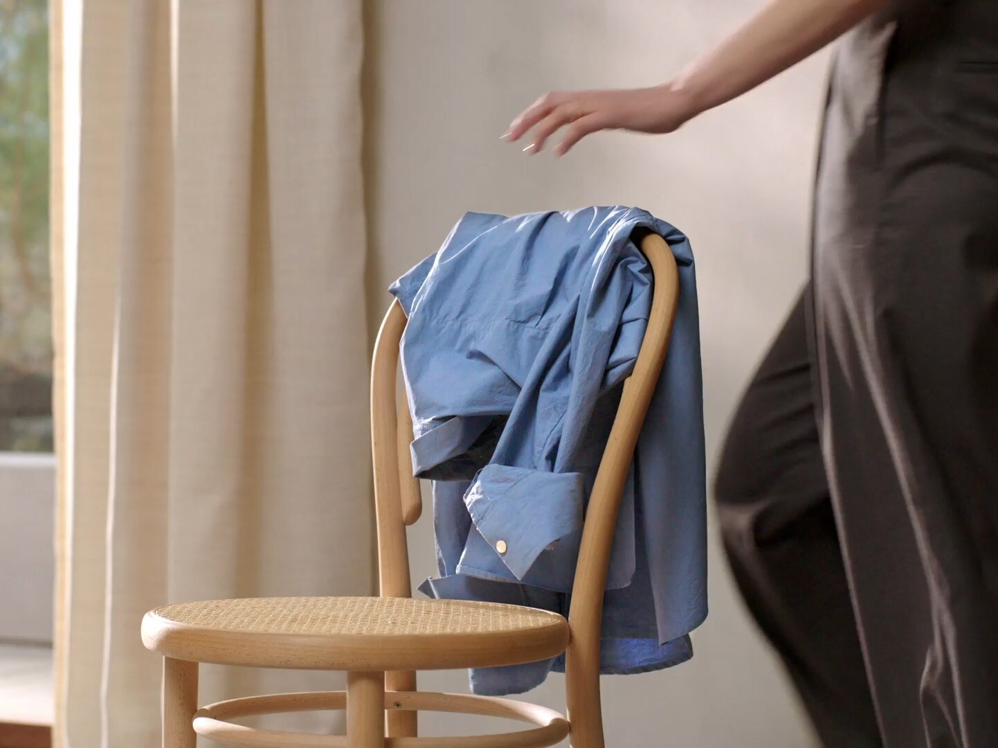 Woman hanging a blue shirt over the back of a chair.